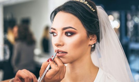 Bride getting professional bridal makeup with soft glam look and veil in a beauty salon