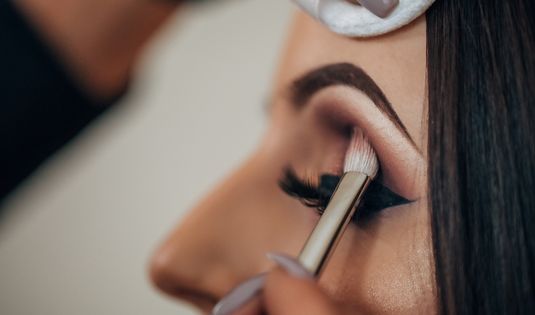 Close-up of a makeup artist applying eyeshadow with a brush on a woman's eyelid for professional eye makeup